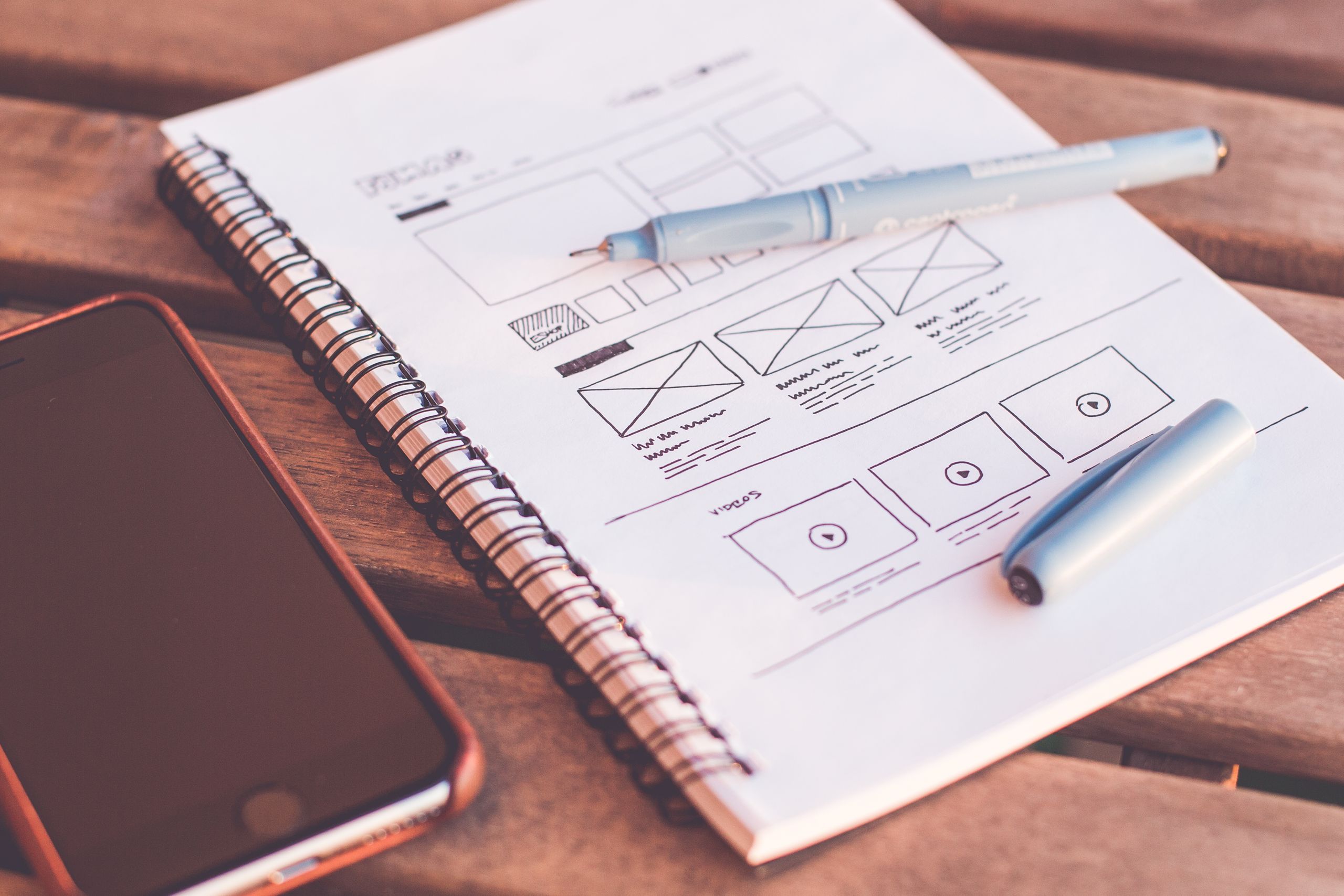 Hand-drawn website wireframe sketches in a notebook beside a pen, representing custom website design
