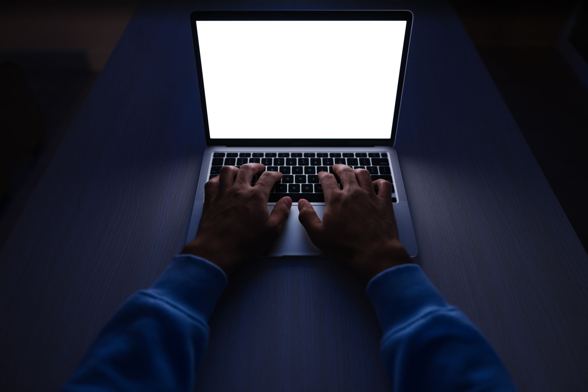 Hands typing on a laptop showing a completely blank white screen in a dark room — the WordPress white screen of death